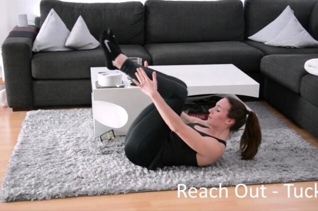 Frau in sportlicher Kleidung führt eine Fitnessübung auf einem Teppich vor einem Sofa aus.