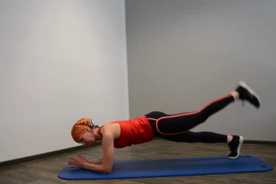 Frau im Plank mit einem Bein gehoben, auf einer blauen Matte in einem minimalistischen Raum.