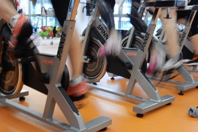 Mehrere Personen trainieren auf Spinning-Bikes in einem Fitnessstudio, die Beine sind in Bewegung.