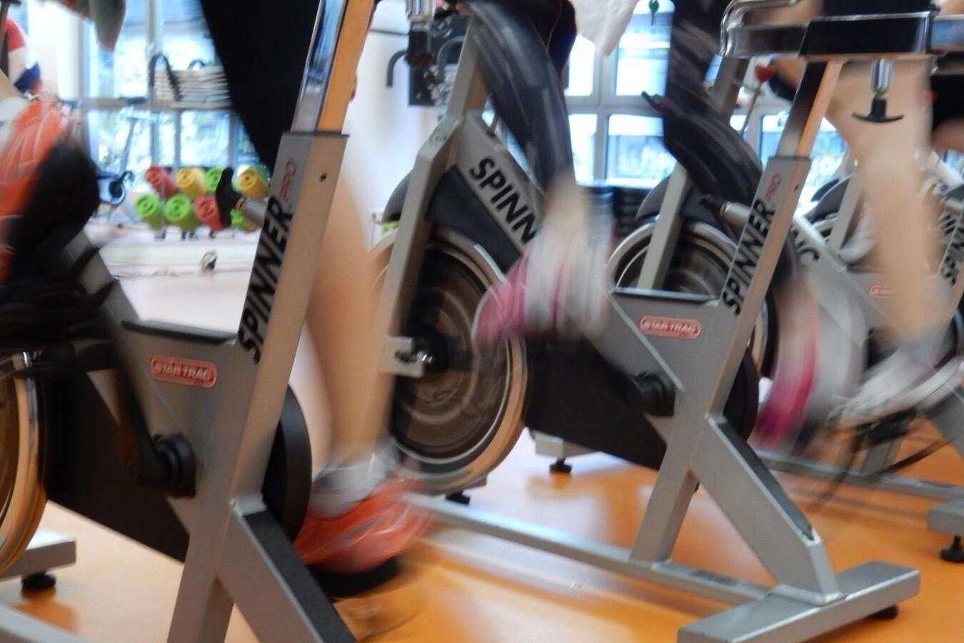 Mehrere Personen trainieren auf Spinning-Bikes in einem Fitnessstudio, die Beine sind in Bewegung.
