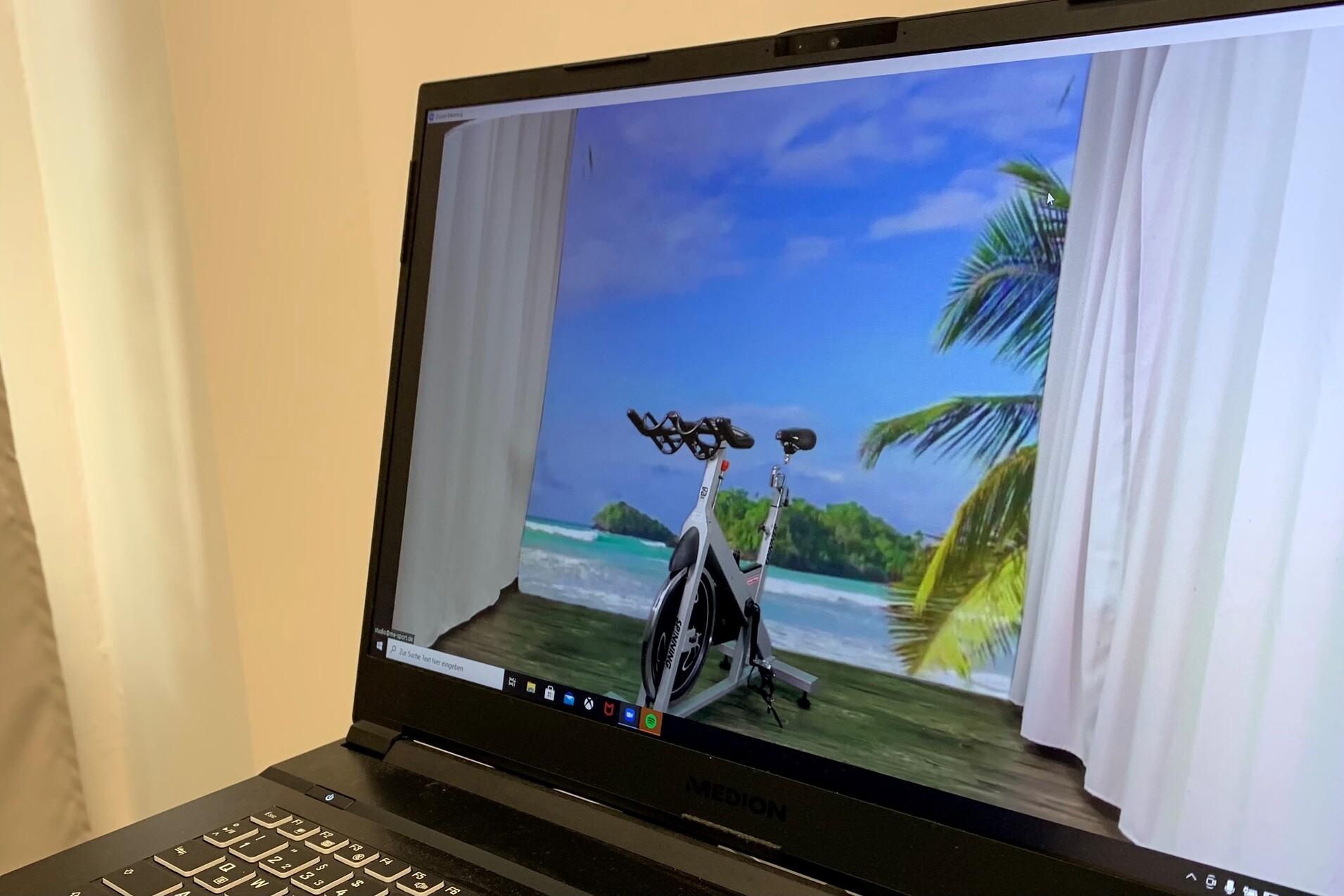 Virtuelles Fitnessgerät steht auf einem Tisch, im Hintergrund eine tropische Strandlandschaft mit Palmen.