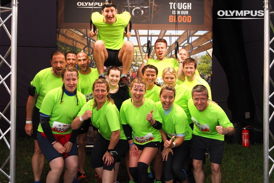 Gruppe von Teilnehmern in leuchtend grünen Shirts, zusammen lächelnd vor einem Banner mit dem Text „TOUGH IS IN OUR BLOOD“.