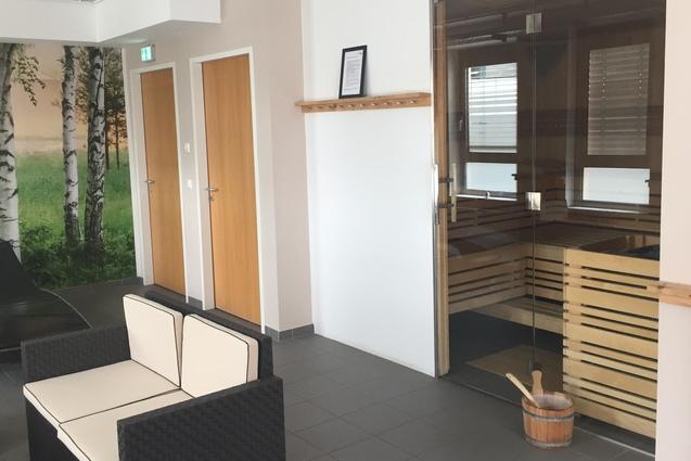 Moderne Wellness-Lounge mit Saunazugang, bequemen schwarz-wei&szlig;en Loungem&ouml;beln und einer Birkenwaldtapete.