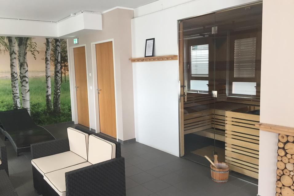 Moderne Wellness-Lounge mit Saunazugang, bequemen schwarz-weißen Loungemöbeln und einer Birkenwaldtapete.