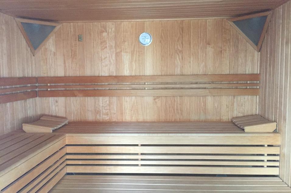 Innenansicht einer Holzsauna mit zwei Bänken und einem Thermometer an der Wand.