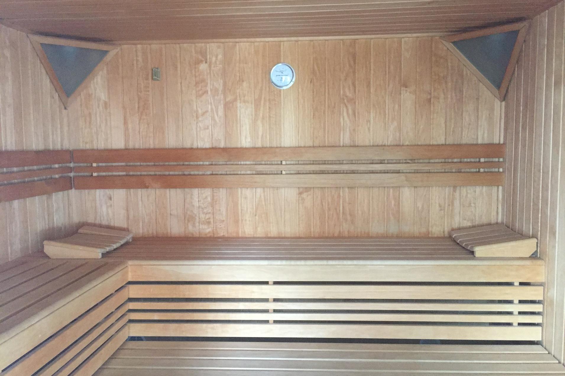Innenansicht einer Holzsauna mit zwei Bänken und einem Thermometer an der Wand.