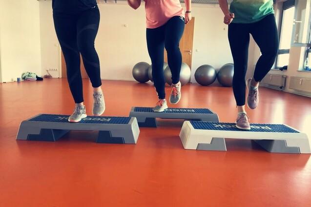 Drei Frauen springen mit Sportschuhen auf Fitness-Stufen in einem hellen, modernen Übungsraum.