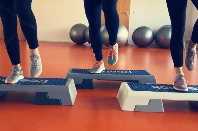 Drei Frauen springen mit Sportschuhen auf Fitness-Stufen in einem hellen, modernen Übungsraum.