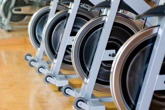 Reihe von Rudergeräten mit Rotationsrädern in einem Fitnessstudio. Holzboden im Hintergrund.