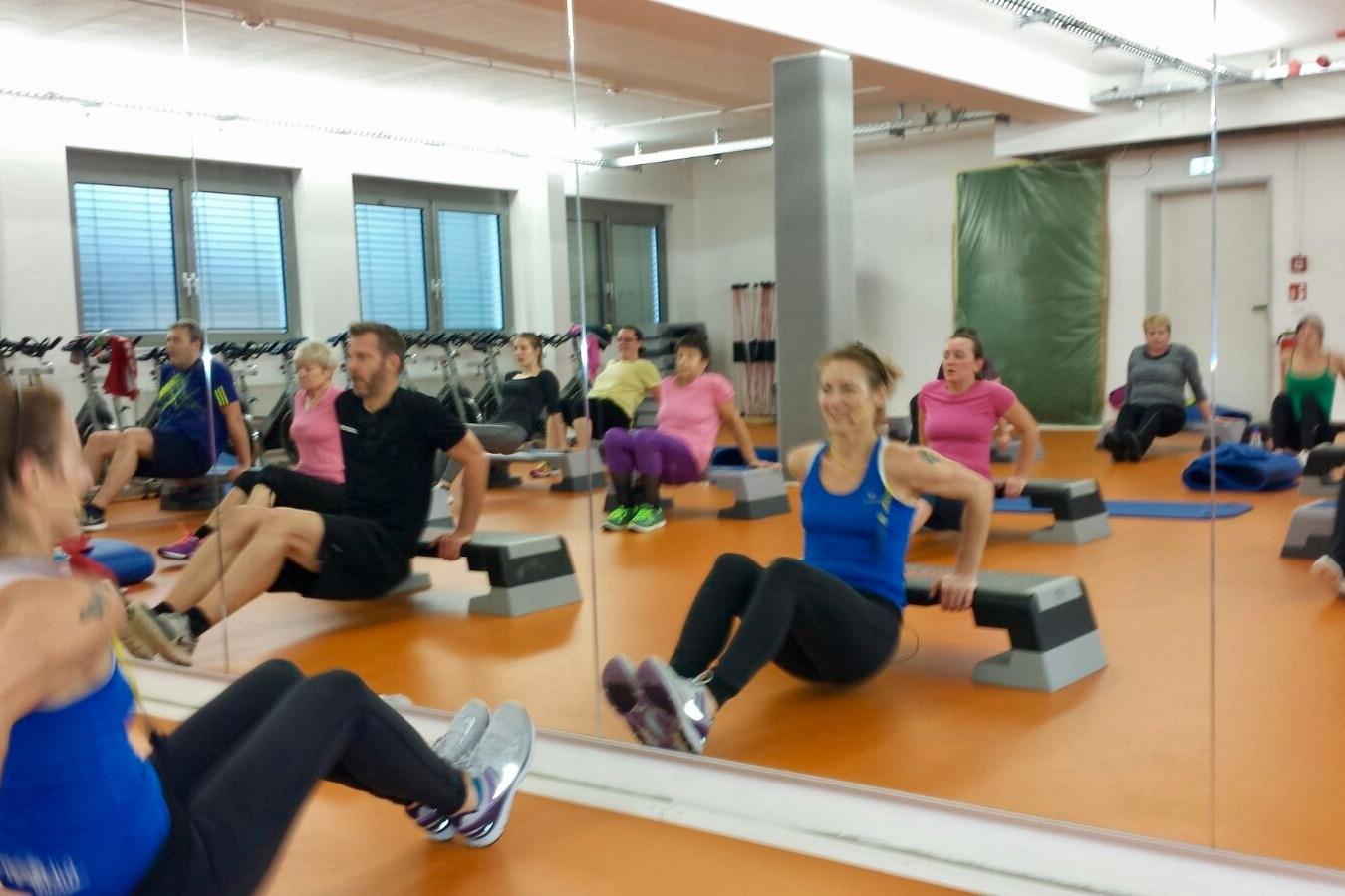 Gruppe von Personen w&auml;hrend eines Fitnesskurses, die auf B&auml;nken Dips ausf&uuml;hren, reflektiert im Spiegel.