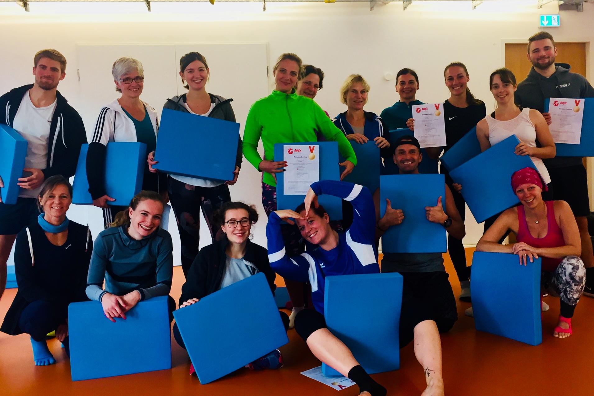 Gruppe von sportlich gekleideten Personen h&auml;lt blaue Platten und Urkunden in einem Raum mit orangefarbenem Boden.