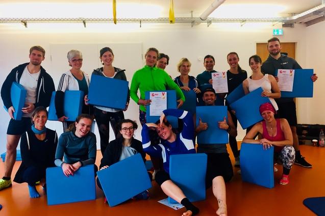 Gruppe von sportlich gekleideten Personen hält blaue Platten und Urkunden in einem Raum mit orangefarbenem Boden.