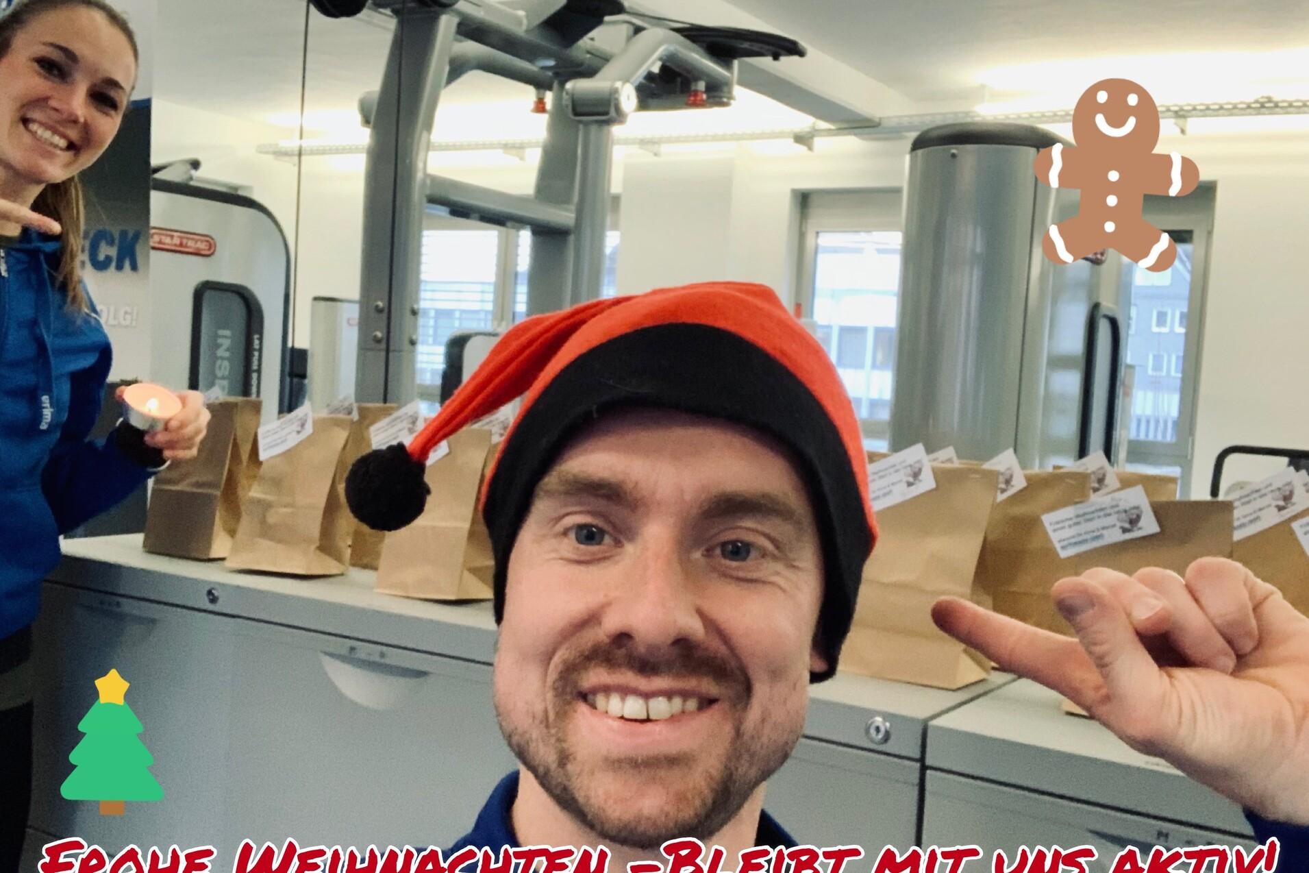 Selbstporträt eines Mannes mit Weihnachtshut und einer Frau im Hintergrund, vor Tüten in einem Fitnessstudio.