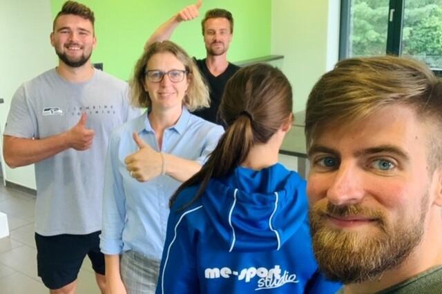 Gruppe von vier Personen, die in einem hellen Raum Daumen hoch zeigen, mit einer Person im Vordergrund im Fokus.