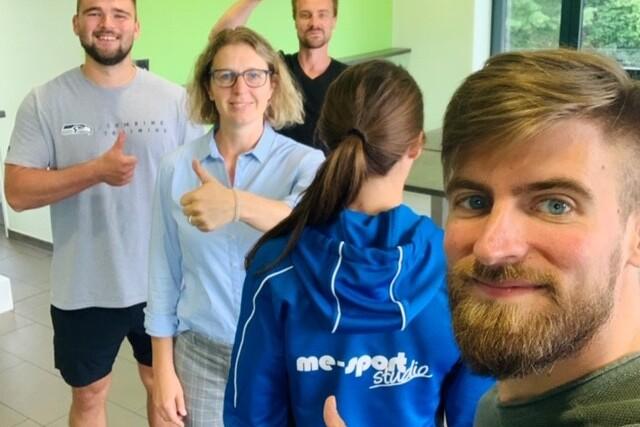 Gruppe von vier Personen, die in einem hellen Raum Daumen hoch zeigen, mit einer Person im Vordergrund im Fokus.